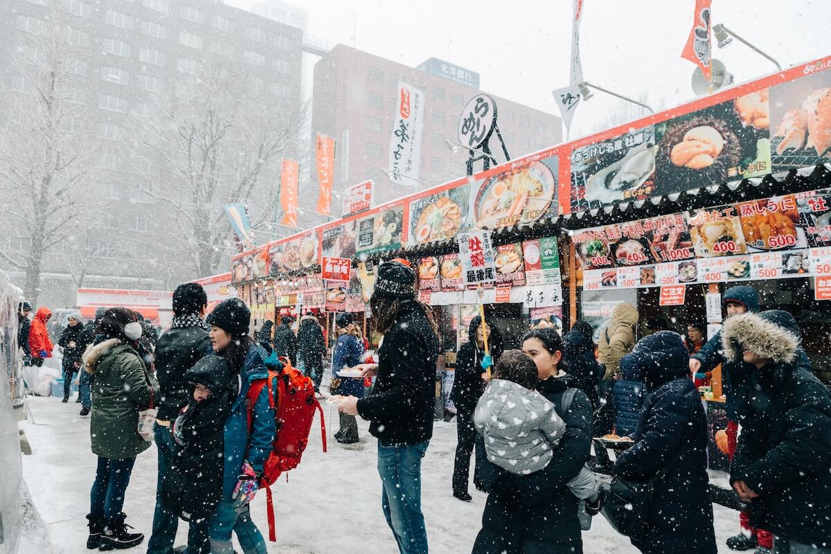 People standing outside food stalls at Sapporo Snow Festival